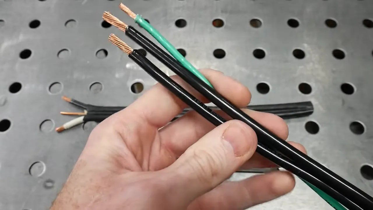 Two black large-gauge conductors and one green grounding conductor held together over a workbench