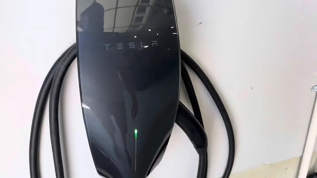 Black Tesla Wall Connector mounted on a garage wall with charging cable coiled around it
