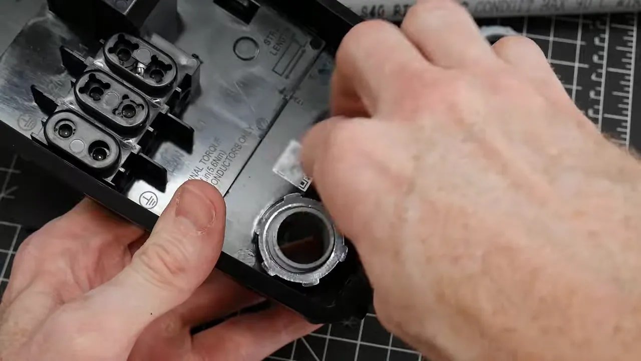Tesla Universal Wall Connector backplate with a gray conduit fitting installed in a rear entry opening