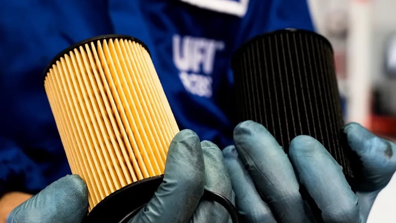 Gloved hands holding a light-colored pleated filter element beside a dark pleated filter element